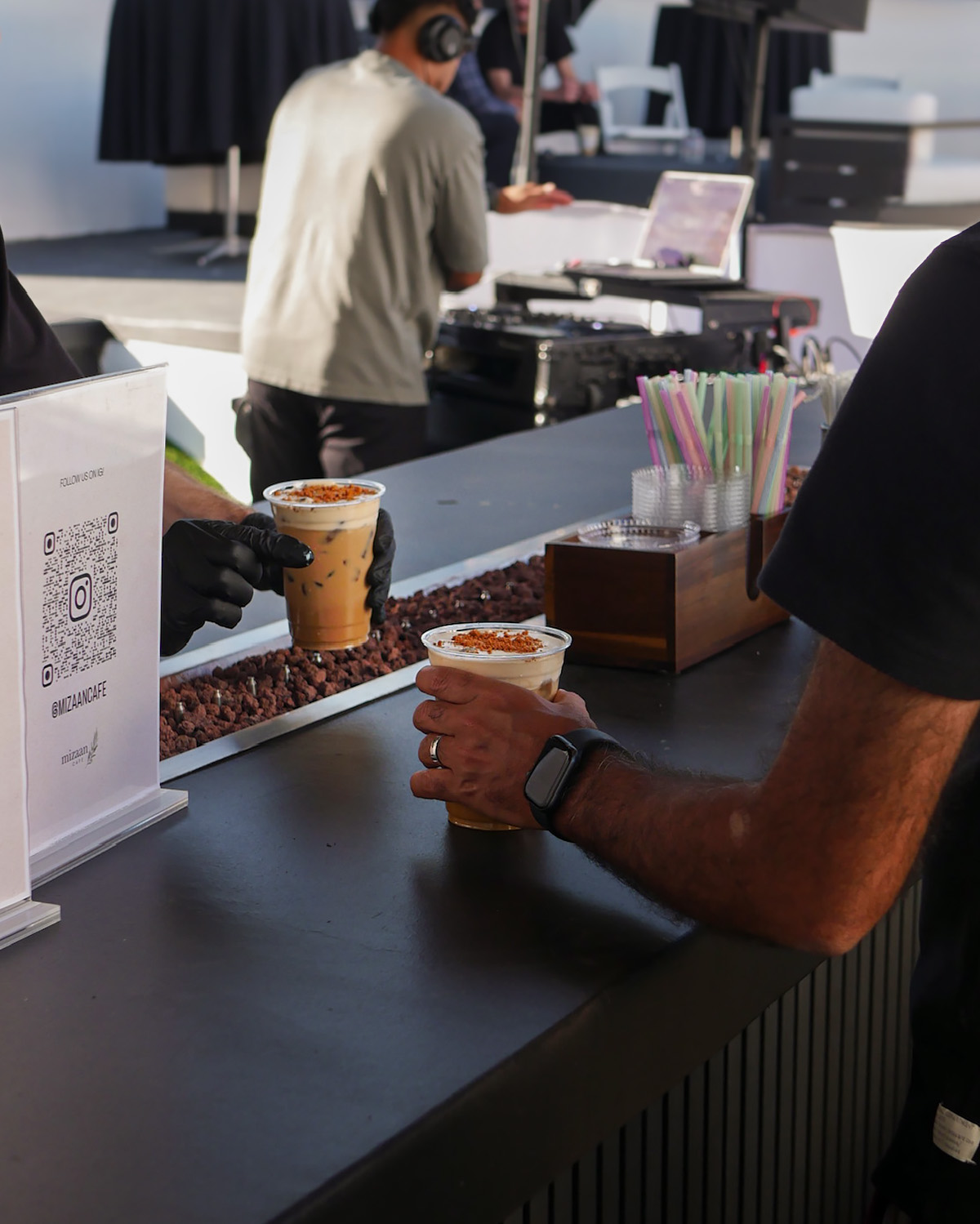 A barista in black gloves hands iced cookie butter lattes to guests across the bar at an event
